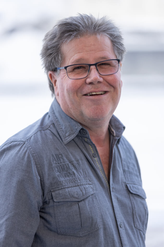 Mann mit Brille und grauem Hemd lächelt, Hintergrund unscharf. SPÖ Kaprun Engagement.