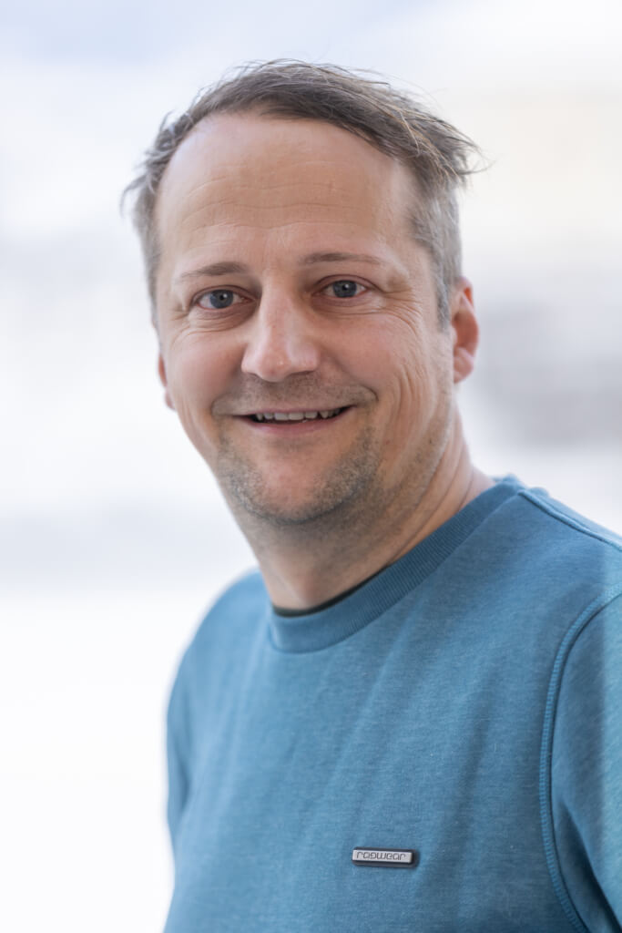 Lächelnder Mann in blauer Kleidung vor hellem Hintergrund, Sympathie für Bürgerengagement.