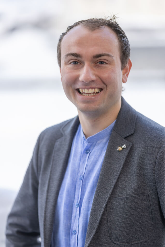 Lächelnder Mann im grauen Blazer vor hellen Hintergrund, verkörpert Bürgerengagement in Kaprun.