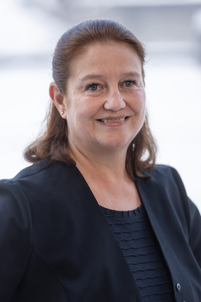 Frau mit kurzer brauner Frisur und schwarzem Blazer lächelt freundlich in die Kamera.