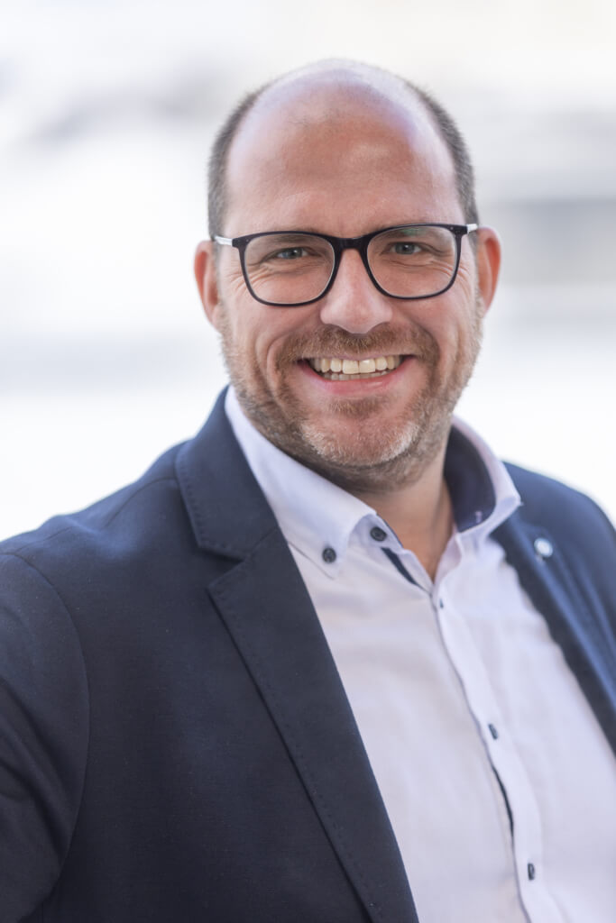 Lächelnder Mann im Anzug, der für soziale Gerechtigkeit und lokale Identität in Kaprun steht.