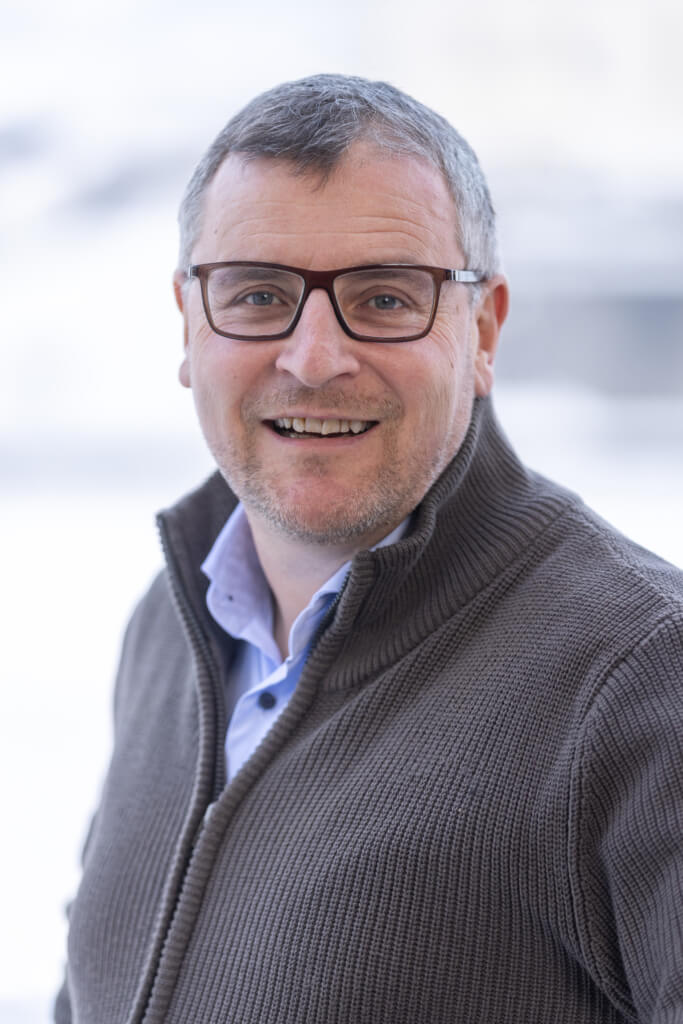 Lächelnder Mann mit Brille trägt einen Pullover, symbolisiert Gemeinschaft in Kaprun.